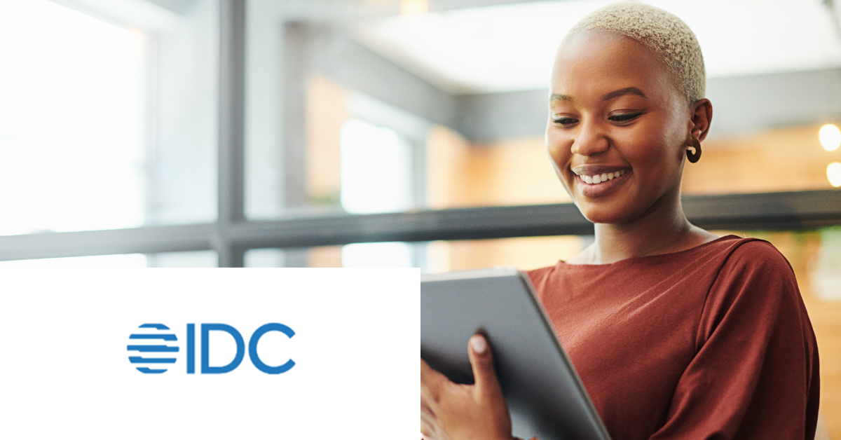 Smiling person holding a tablet indoors with IDC logo in the corner.