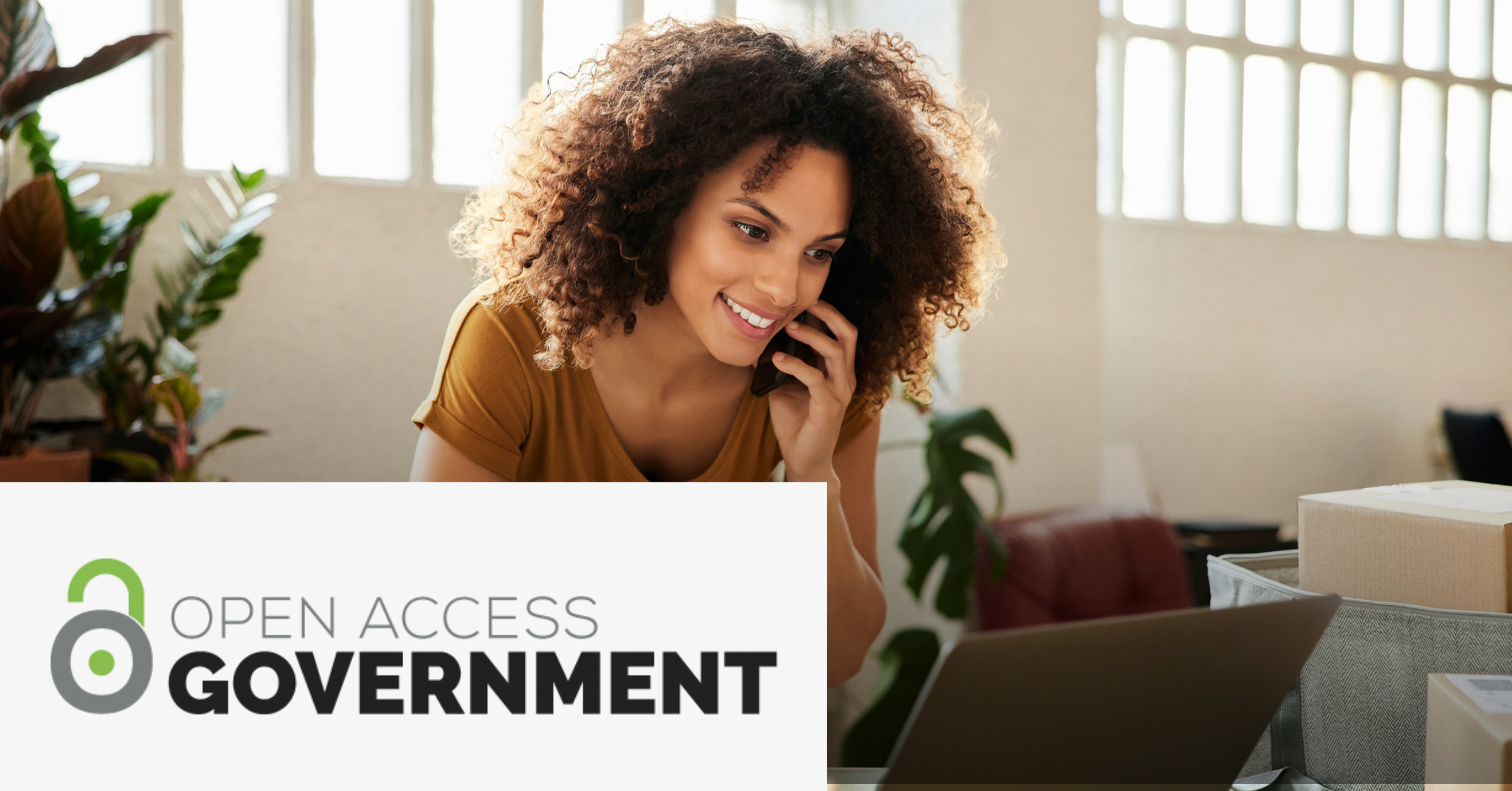 Image of a woman using her phone while consulting information on the screen of a laptop. On the lower left corner is placed the Open Access Government logo.
