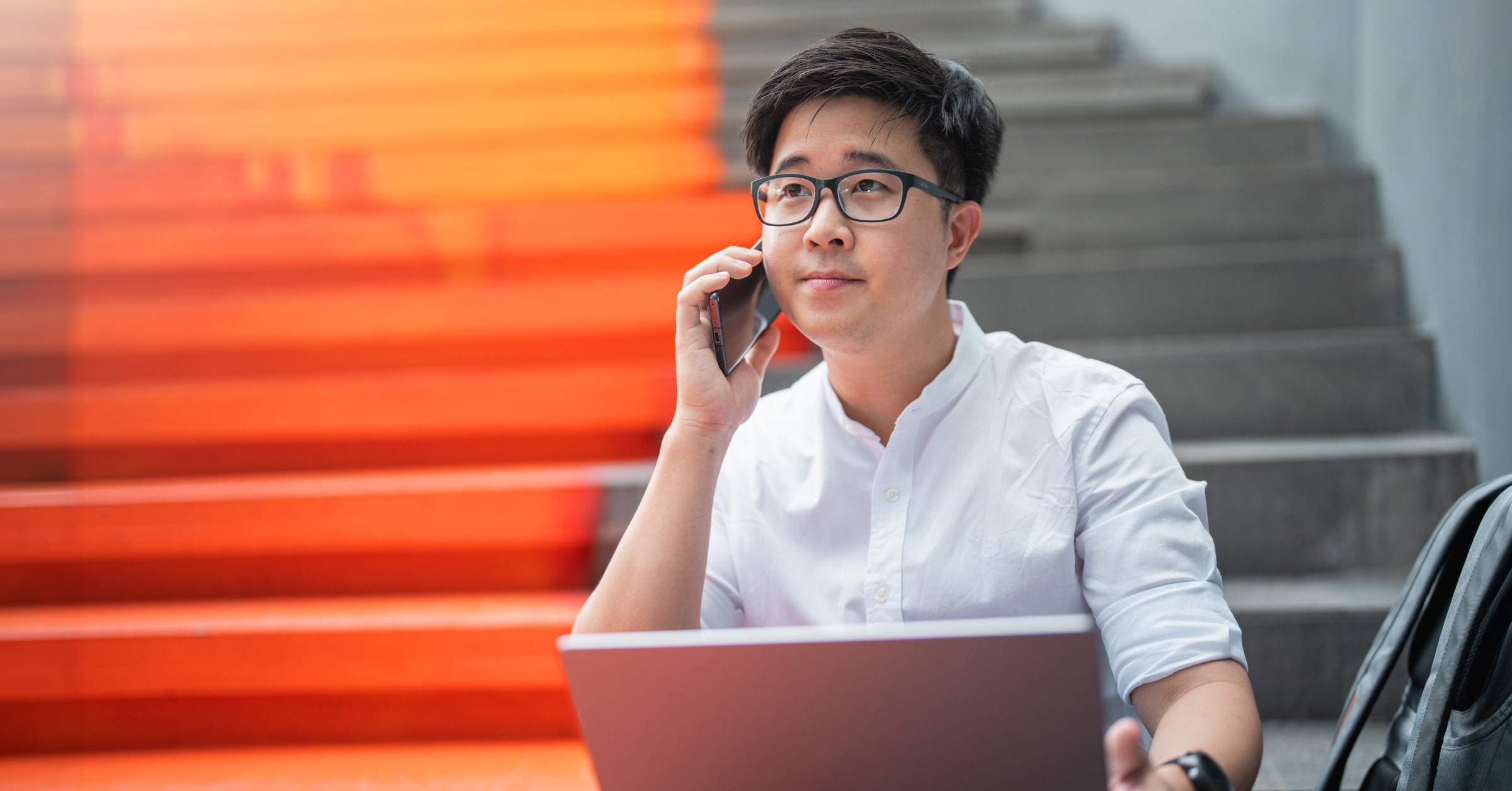 Photo of a person sitting on steps talking on the phone with a laptop in their lap