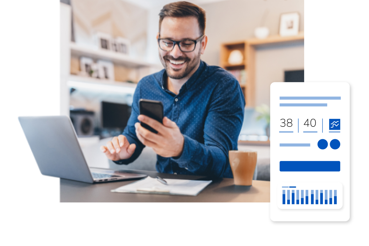 Smiling man looking at his phone while working on a laptop at a desk