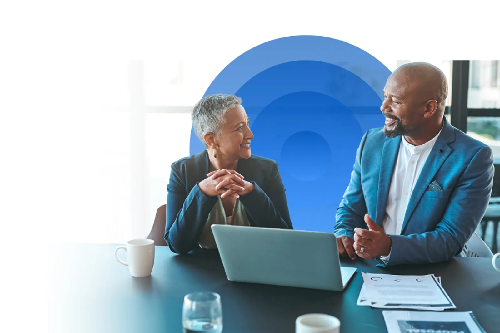 Photo of two people talking while working at a laptop